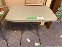 Side view showing the foldable metal legs and beige plastic top with label indicating dimensions 30"L x 19"D x 28"H.
