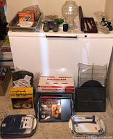 All items arranged on and in front of a freezer, showing bakeware, baking dishes, cutting tools, glass containers, and napkin holders.