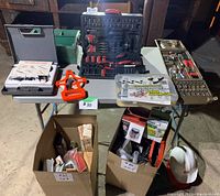Various toolboxes and tools displayed on a table including toolkits, hard hats, hardware box, and cardboard boxes with assorted items