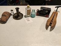 Photo showing the full lot of vintage and antique items placed on a white surface including wooden shoe stretchers, toy cars, bottles, and a candle holder.