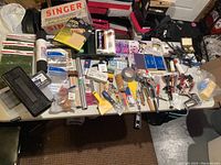 Overview of the entire lot of mixed arts and crafts materials including boxes, bags, rolls, and various small tools on a white table.