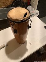 Full view of wooden bongo drum showing torn and worn drum skin on top and natural wood finish body with metal tuning brackets attached.