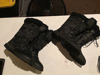 Two black Canadiana winter boots with fur lining around ankle cuff, rugged soles shown in side and bottom view.