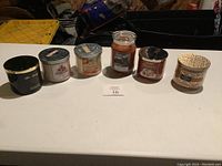 Six candles on white table, various brands and scents, all new and unlit.