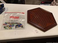 Photo of the hexagonal wooden Chinese Checkers game board and a plastic bag containing assorted colored glass marbles.