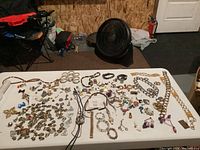 Overview of the entire lot on a white table showing diverse jewelry including rings, pins, charms, chains, and pendants scattered and laid out.