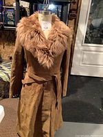 Front view of a long brown leather coat with a wide light brown fur collar and matching belt, displayed on a mannequin.