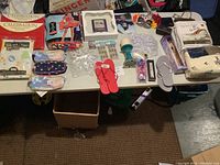 Assorted household items on table including tablecloths, costume, flip-flops, eyeglass cases, crystal figurines, toiletries, and pens.