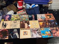 Photo showing a collection of vinyl records arranged on a table with various album covers visible including Bob Marley, Oklahoma soundtrack, Survivor, and more.
