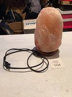 Front view of the rough-cut pink Himalayan salt lamp on wooden base, power cord coiled beside it.