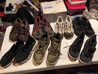 Wide angle showing 7 pairs of shoes in various conditions on white surface.