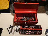 Red metal toolbox with lid open showing assorted tools inside and a lower tray full of sockets.