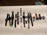 All 12 watches laid out on a beige surface, showing mixed styles and bands.