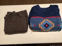 Two folded wool sweaters displayed, one brown and one blue with a geometric pattern