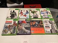 Nine Xbox 360 game cases displayed on table, front covers visible including Call of Duty, Tiger Woods PGA Tour, NBA Live, NHL Series, and others.