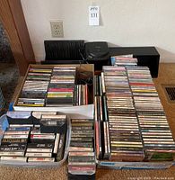 Wide shot showing the portable CD player with wired headphones, large stacks of DVDs in cases, cassette tapes in cases, and two black plastic organizers.