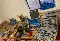 Wide view of workbench showing various hand tools laid out, including tool kits, cases and individual tools