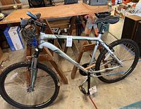 Side view of thigh silver and green Raleigh Talus 3.0 mountain bike showing frame, suspension fork, tires, and accessories including lock, pump and headlight.