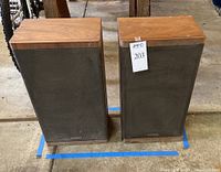 Pair of vintage Optimus Pro 300 speakers shown side by side with wood veneer tops and black front fabric grills, dusty with visible wear.