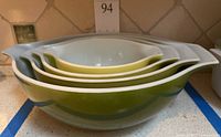 Side view of the set of four Pyrex nesting bowls showing size gradient and color transition from yellow to avocado green.