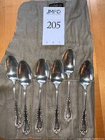 Six spoons arranged on a cloth roll with lot sign