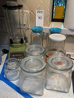 Image showing Waring olive green blender base with ribbed glass jar and black lid, three square glass jars and other glass containers positioned around.