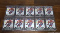 Photo showing all 10 Cole Caufield rookie hockey cards laid out in two rows of five on a wooden surface.
