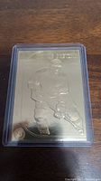 Front side of the card showing an embossed image of Wayne Gretzky in hockey gear on reflective gold surface, in protective plastic.