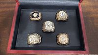 Top view of all five Edmonton Oilers replica Stanley Cup rings arranged in a box, displaying their gold tone and simulated diamond-like stones.