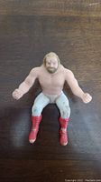 Front view of the LJN Big John Stud thumb wrestler figure showing muscular upper body, blonde hair, white tights, and red boots with some paint wear.