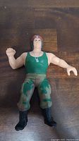 Front view of LJN Corporal Kirchner action figure. Green tank top, camo pants, black boots, red beret.