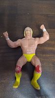 Front view of LJN Hulk Hogan action figure lying on a wooden surface showing muscular build, yellow trunks, boots, and wrist tape.
