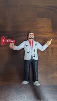 Front view of the Jimmy Hart action figure showing the figure's face, white jacket with musical notes design, black pants, and red megaphone.