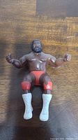 Front view of the LJN Junkyard Dog thumb wrestler figure showing figure seated position with red trunks, knee pads and white boots.
