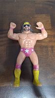Front view of vintage LJN Macho Man Randy Savage action figure lying on wood surface showing muscular build and detailed paint.