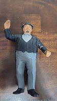 Front view of the vintage LJN Mr. Fuji wrestling action figure showing the painted face, black jacket, light blue shirt, gray pants, and black shoes, with the right arm raised.
