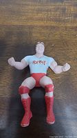 Front view of Rowdy Roddy Piper thumb wrestler figure showing white T-shirt with red lettering and red boots and knee pads.
