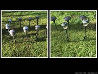 Photo of ten silver metal stake solar landscaping lights with tiered mushroom-shaped tops arranged on grass outdoors.