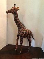 Photo of large giraffe figurine standing upright, showcasing its painted spots and anatomy with some signs of repair.