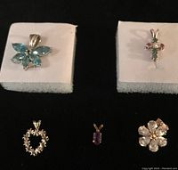 Five assorted gemstone pendants displayed on white and black foam pads with a dark background.