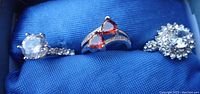 Three rings displayed side by side on blue fabric background showing gemstone and band details.