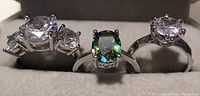 Photo of three rings with large gemstones, two clear and one multicolored, all set in silver-tone metal bands with prong settings.
