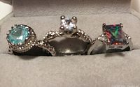 Photo showing three decorative rings inside a jewelry box, each with different colorful gemstones and band designs.