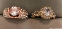 Photo showing two rings with central clear gemstones and surrounding smaller stones, one rose gold-toned with multiple rows along the band, the other gold-toned with a halo setting.