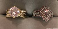 Photo of two rings featuring prominent pink stones on decorative split shank bands, one gold-tone and one silver-tone.