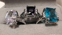 Photo of three rings set side by side on a gray felt holder, showcasing their colored stones and side accents.