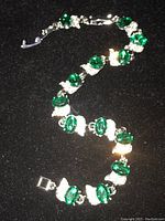Photo showing silver-tone necklace with several green oval gems and clusters of clear rhinestone crystals on a black background.