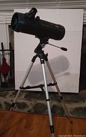 Photo of black Newtonian reflector telescope mounted on silver and wood tripod with handle for aiming adjustments.