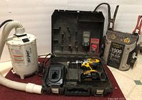 Mixed tools including Stryker Glide vacuum, DEWALT cordless drill in case with charger, Stanley Jump It jump starter, and two digital multimeters arranged together.