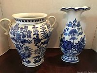 Photo showing two blue and white porcelain vases with floral and willow designs, one urn-shaped with handles and one tall with fluted rim.